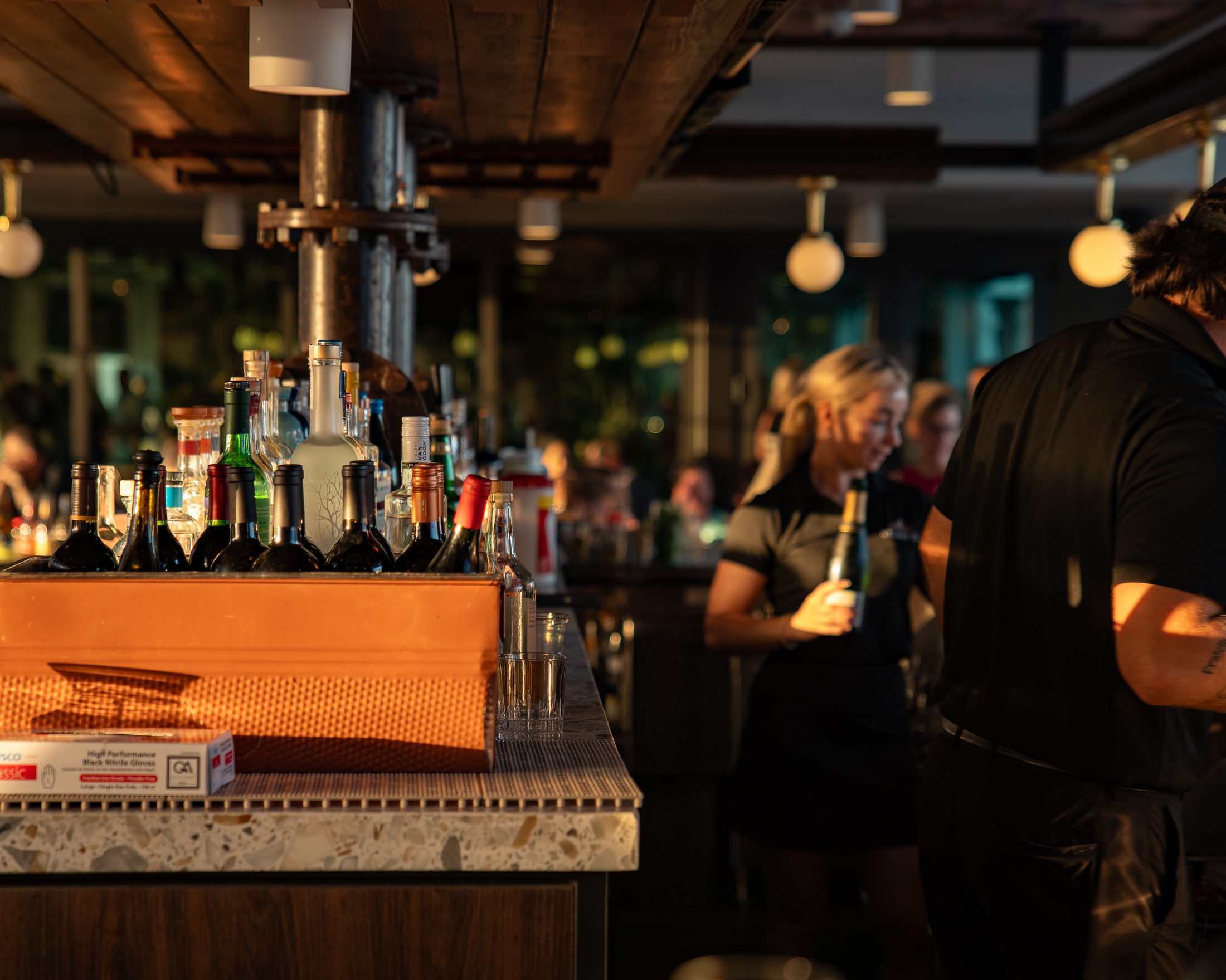 Warm bar service detail with guests and staff inside a hospitality venue